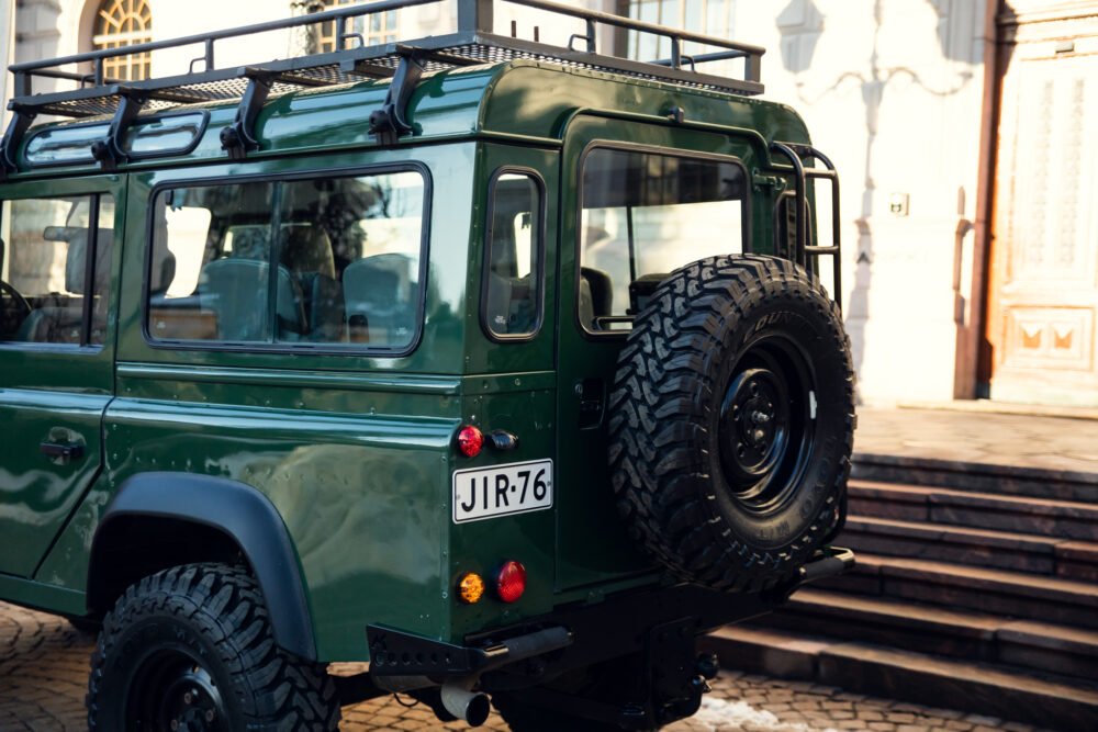 Green vintage SUV parked on cobblestone street.