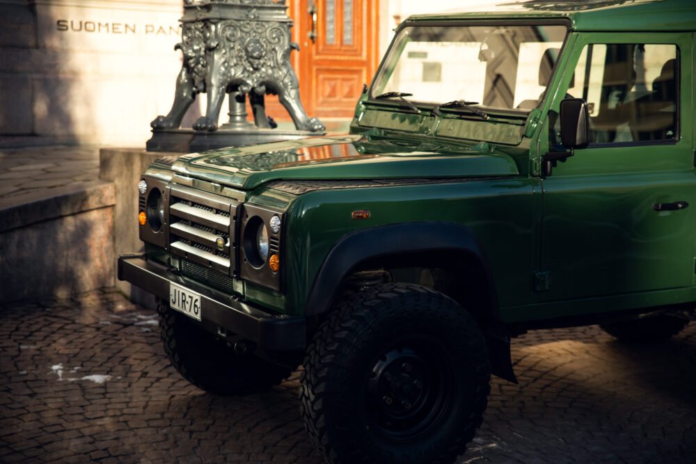 Green off-road vehicle parked by historic building.