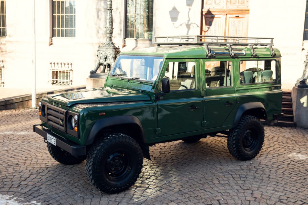 Green SUV parked on cobblestone street near historic building.