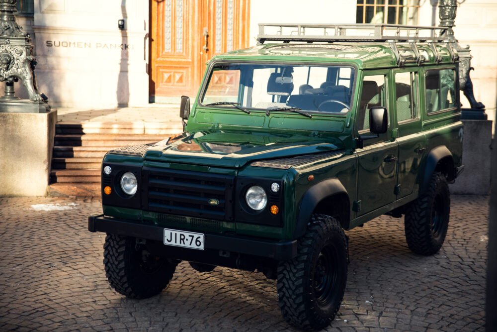 Green off-road vehicle parked outside elegant building.