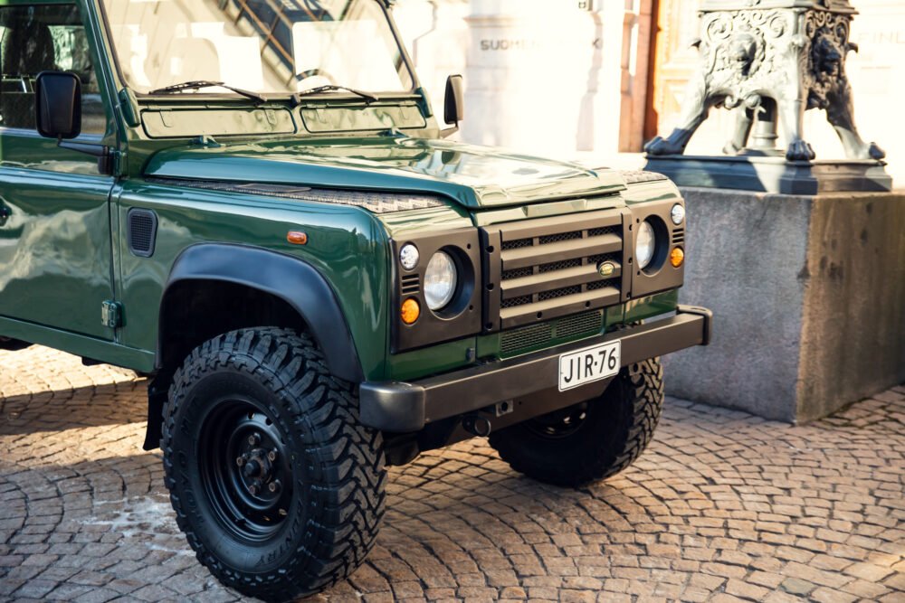 Green Land Rover parked beside historic statue.