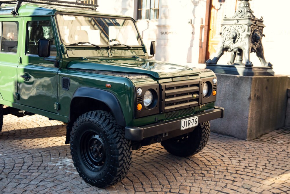 Green Land Rover Defender parked near ornate fountain.