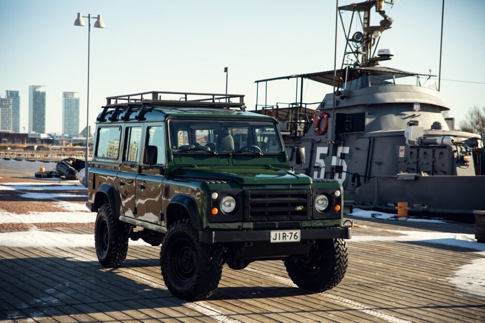 Green SUV near ship on urban waterfront dock.