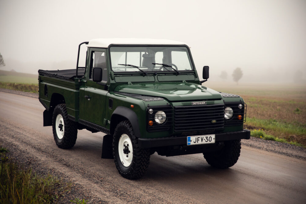 Green Land Rover Defender on foggy road.