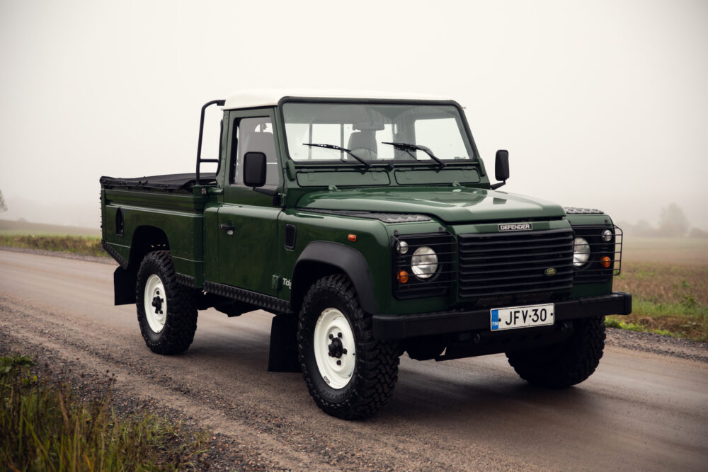 Green Land Rover Defender on misty road.