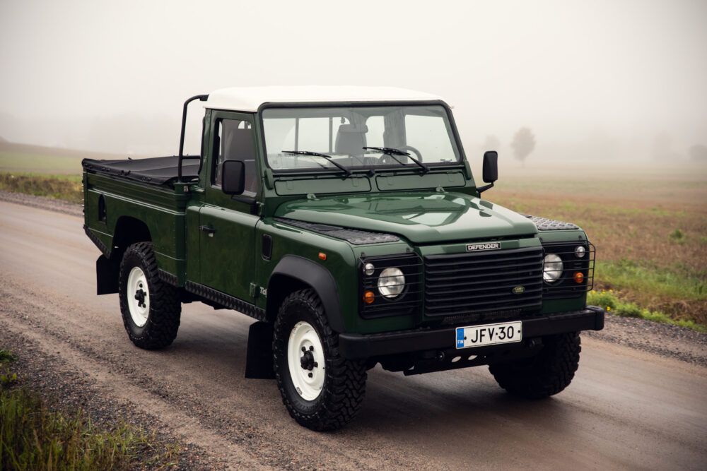 Green Land Rover Defender on foggy country road.