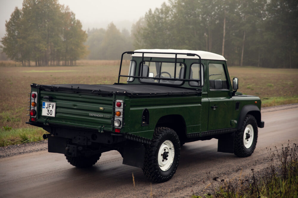 Green Land Rover Defender on misty rural road.