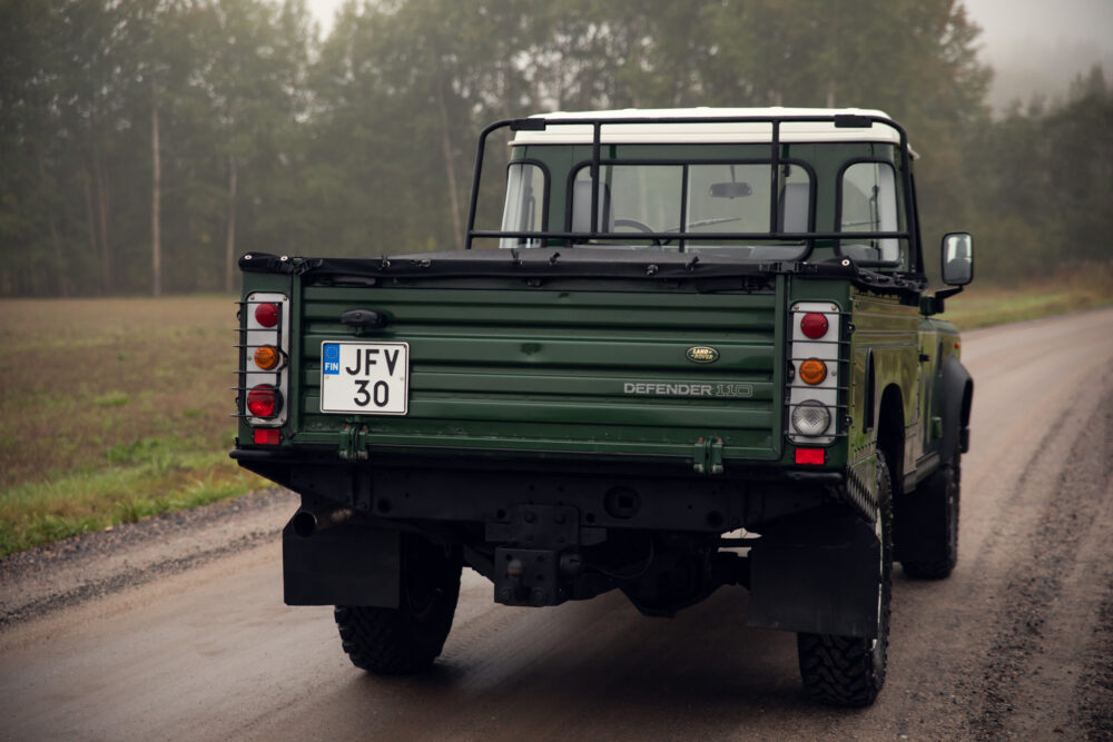 Green Land Rover Defender on foggy road.