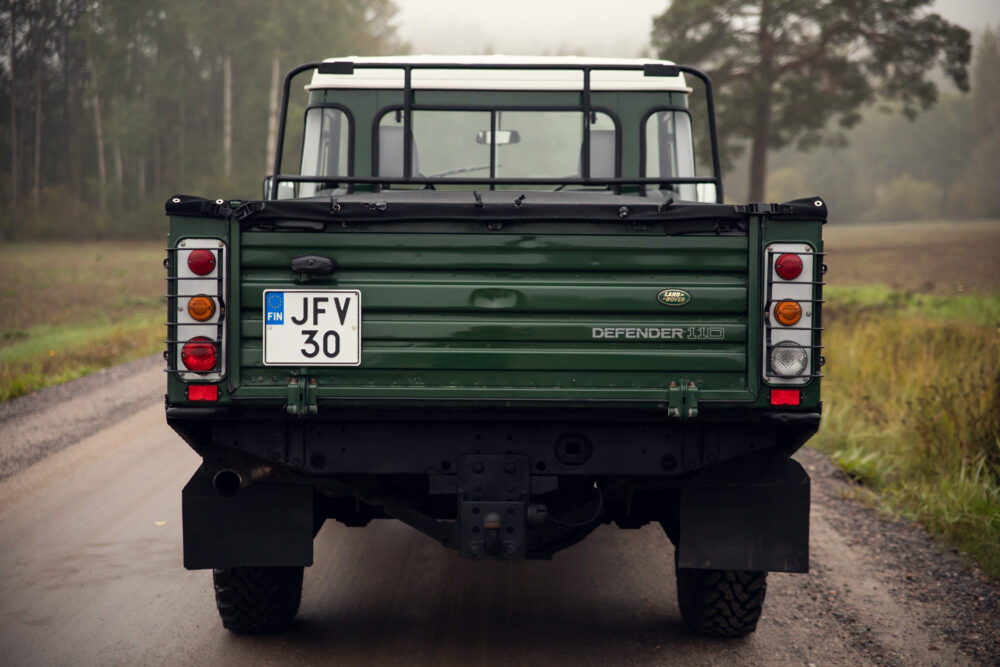 Green Land Rover Defender 110 on foggy rural road.