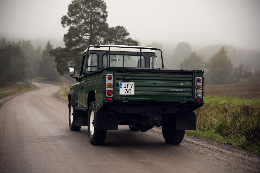 Green Land Rover Defender on foggy rural road.