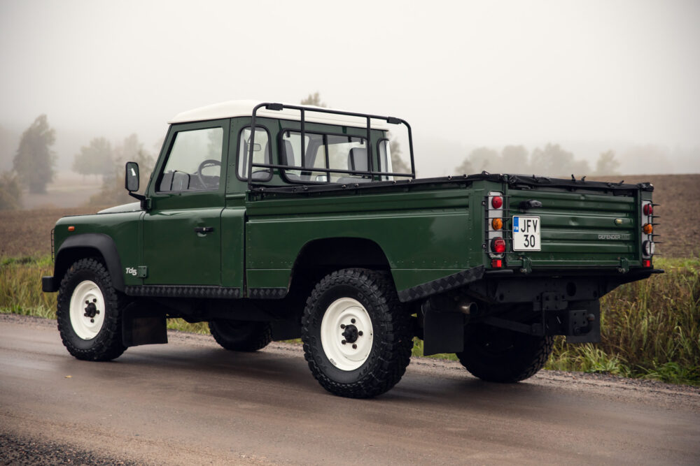 Green Land Rover Defender on foggy rural road.