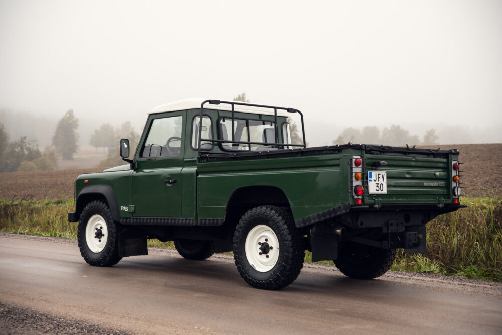 Green Land Rover Defender on foggy rural road.