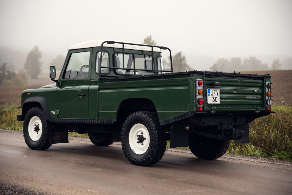 Green Land Rover Defender on foggy rural road.