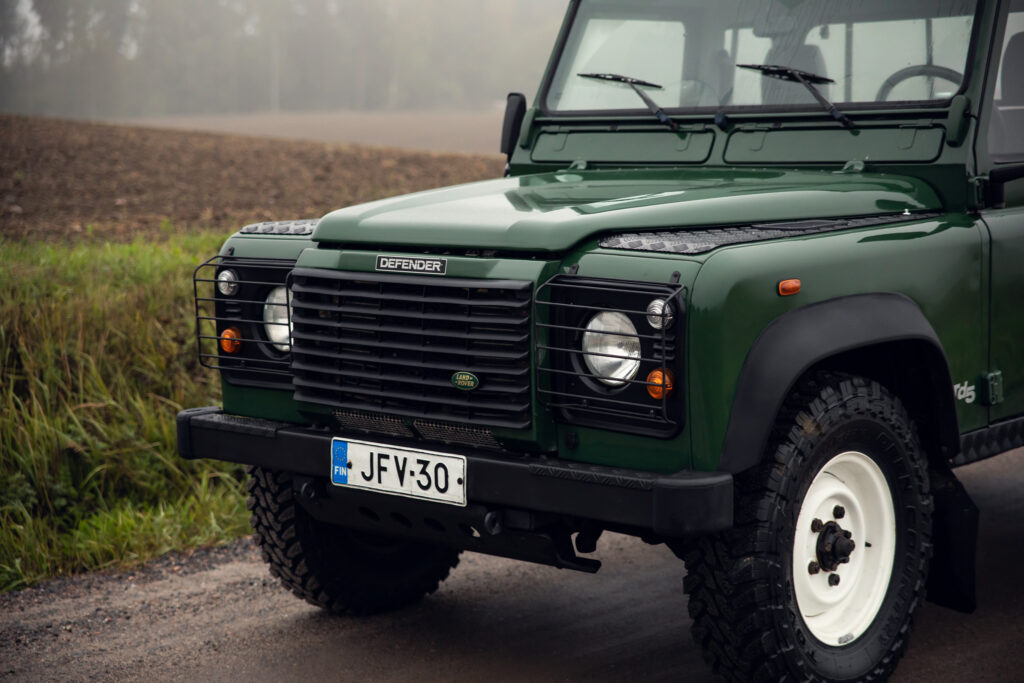 Green Land Rover Defender on foggy road.