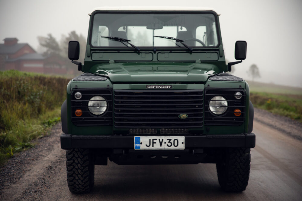 Green Land Rover Defender on foggy rural road.