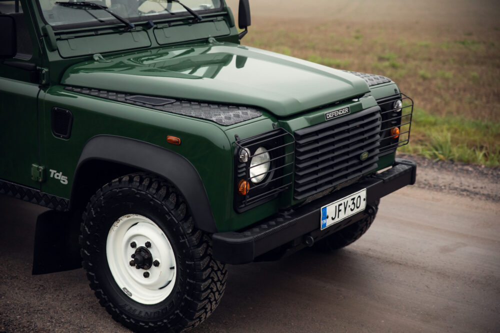 Green Land Rover Defender on wet road.