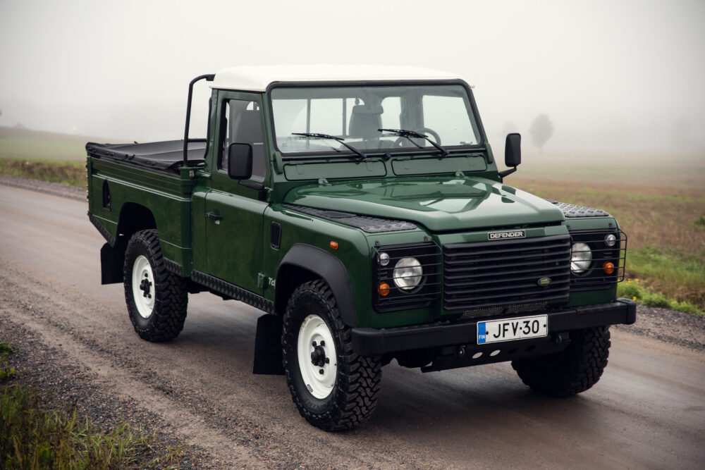 Green Land Rover Defender on foggy road.