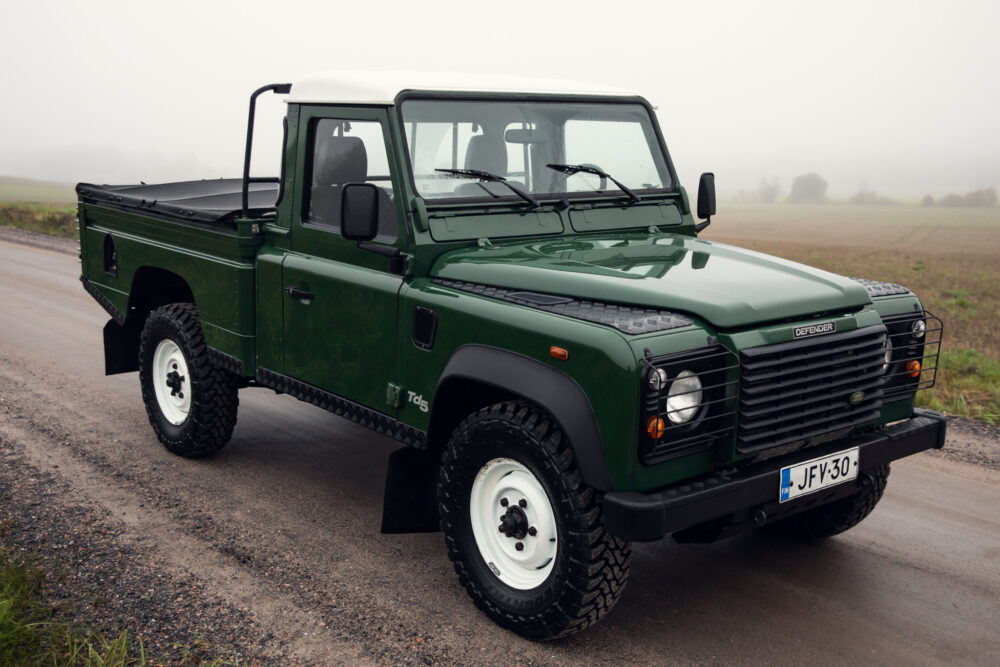 Green Land Rover Defender on foggy rural road.