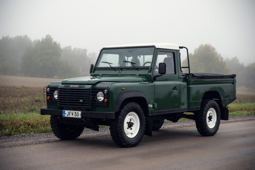 Green Land Rover Defender on foggy rural road.