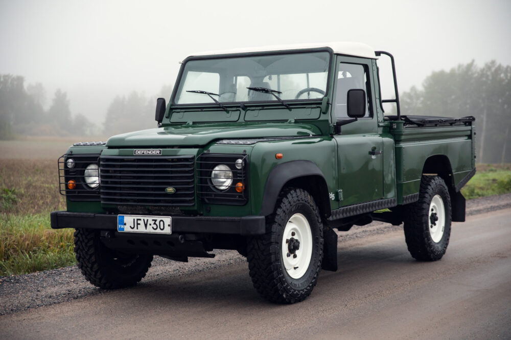 Green Land Rover Defender on foggy country road.