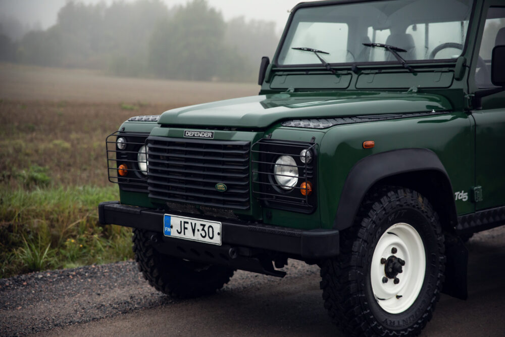 Green Land Rover Defender in misty field.