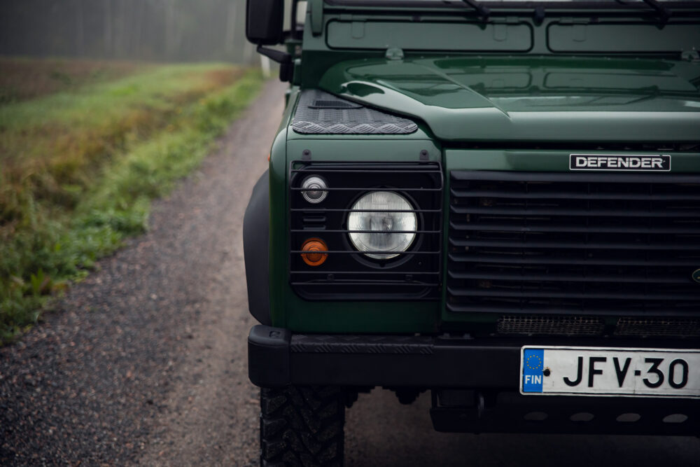 Green Land Rover Defender on foggy forest road.