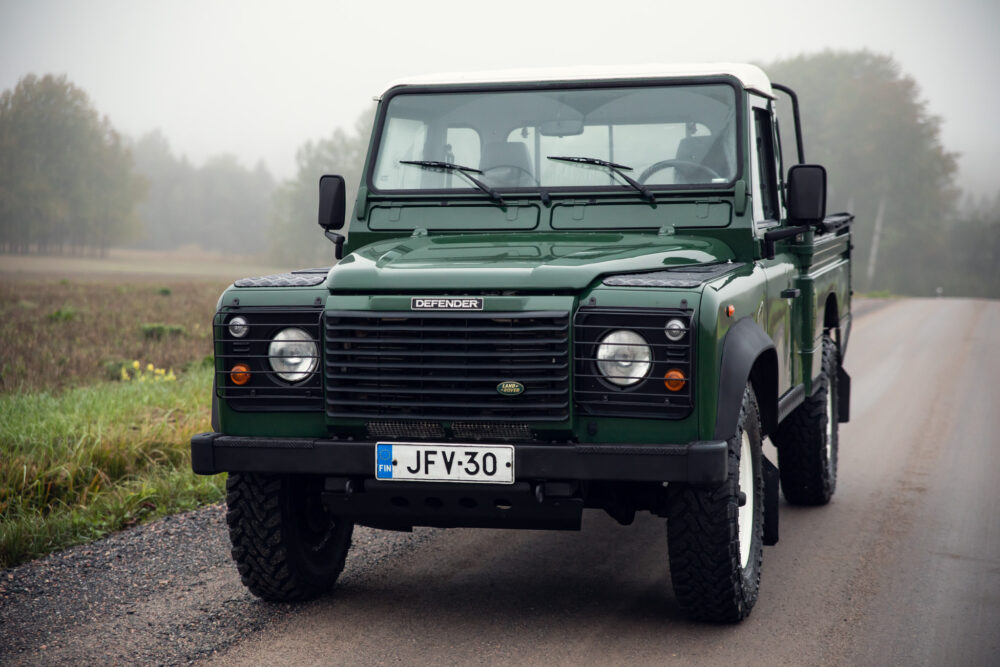 Green Land Rover Defender on foggy rural road.