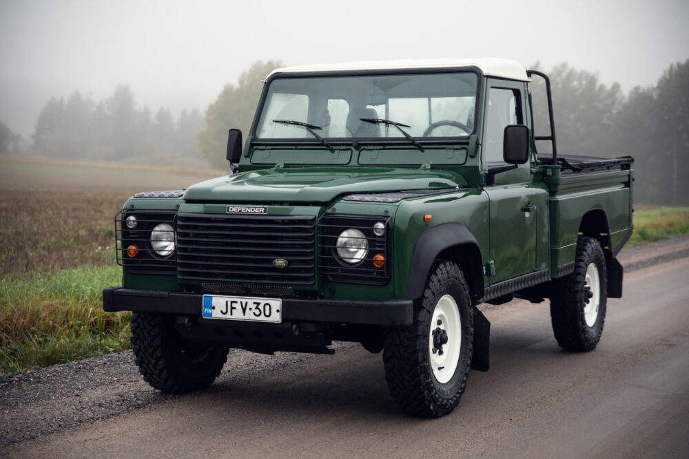 Green Land Rover Defender on foggy rural road.