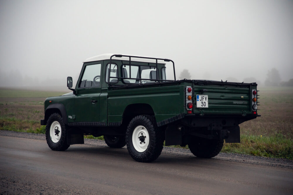 Green Land Rover Defender on foggy rural road.