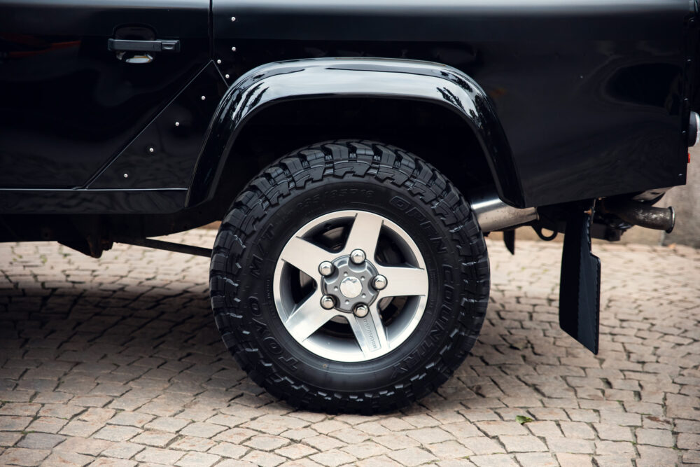 Black truck's tire on cobblestone surface.