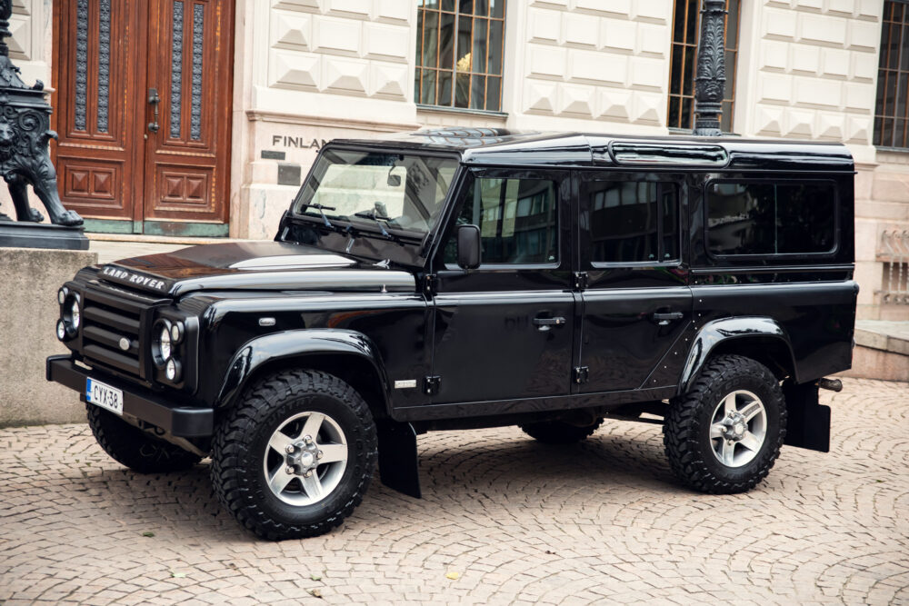 Black Land Rover Defender parked near historic building.