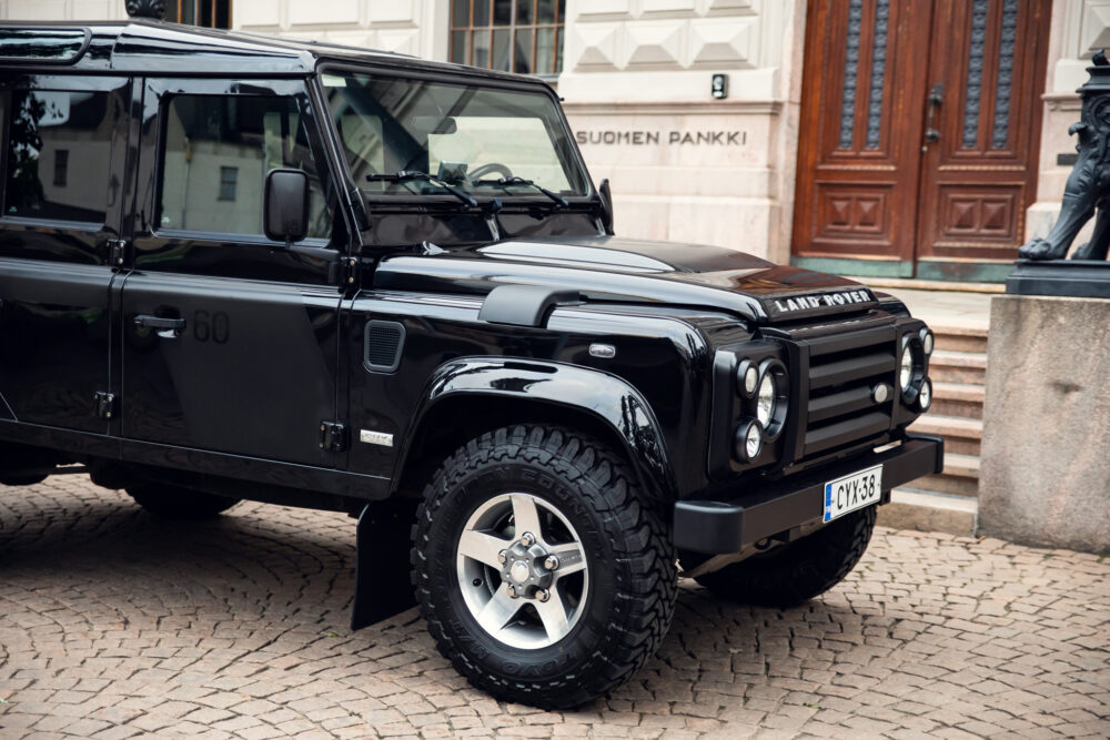 Black Land Rover Defender parked by historic building.