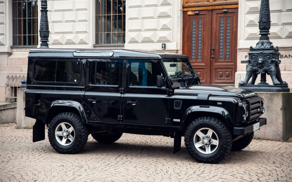 Black SUV parked near historical building on cobblestone street.