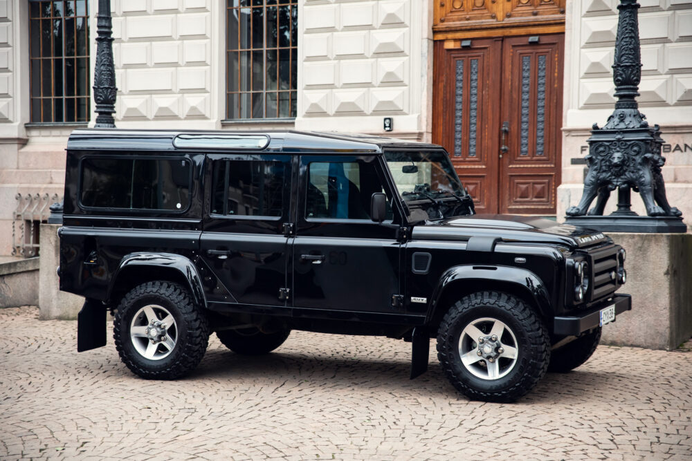 Black SUV parked near historical building on cobblestone street.