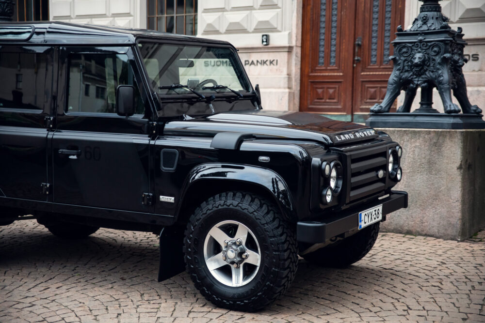 Black Land Rover Defender parked near historic building.