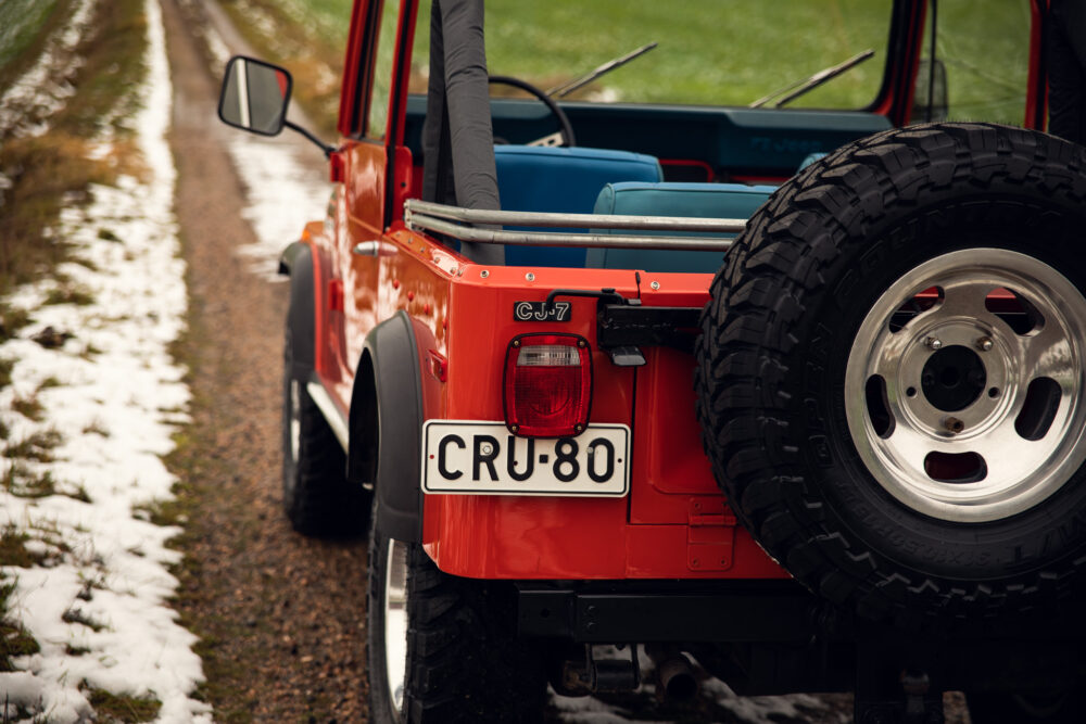 Red Jeep CJ-7 with spare tire on snowy trail