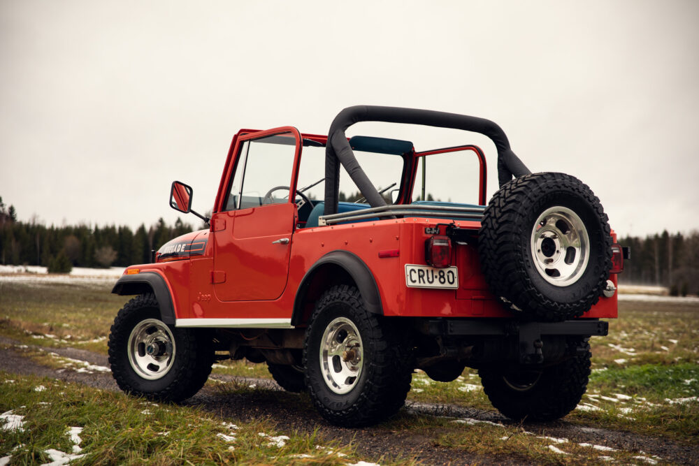 Red Jeep parked outdoors on snowy grassland.