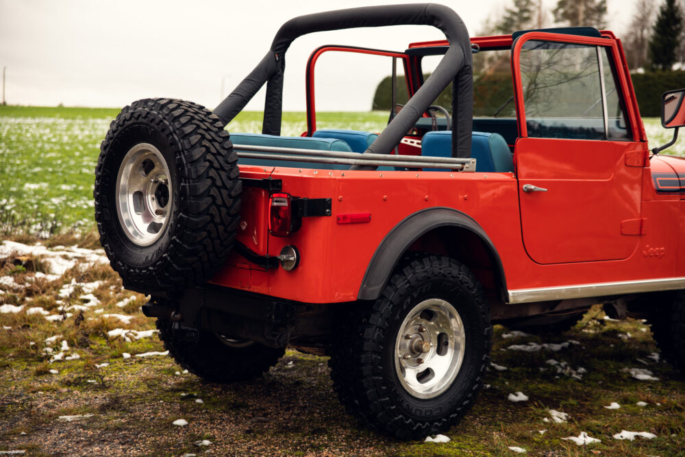 Red jeep parked on grass with snow patches