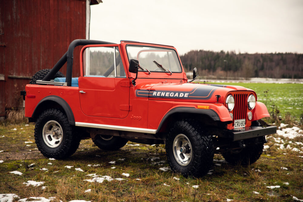 Red Jeep Renegade parked near barn on snowy ground