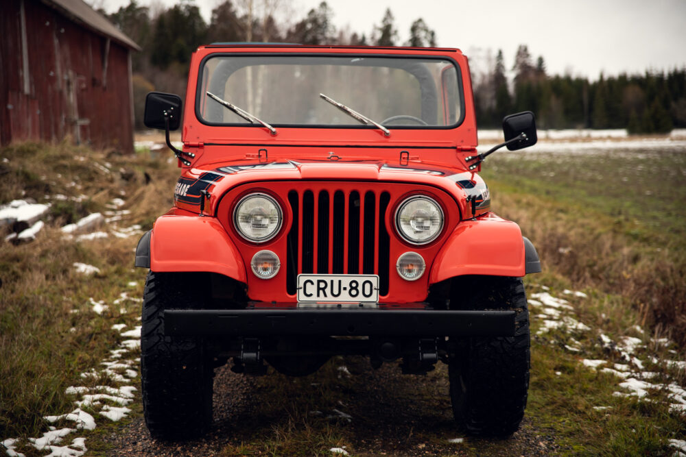 Red vintage jeep parked near wooden barn in winter