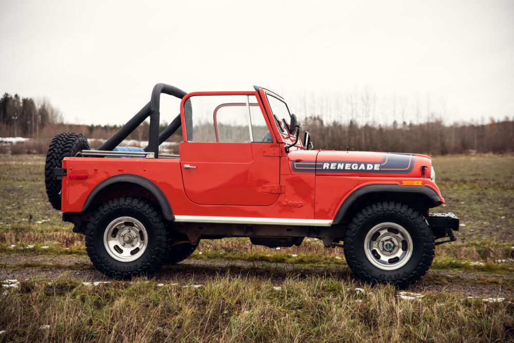 Red Jeep Renegade convertible parked in muddy field.