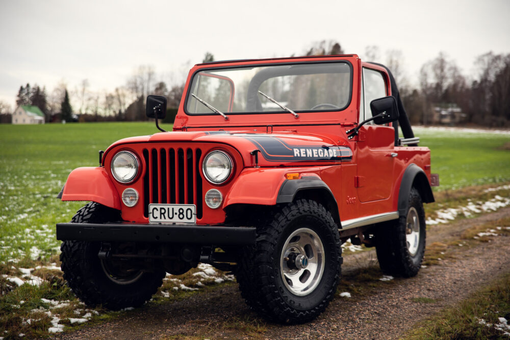 Red vintage jeep on green field with light snow