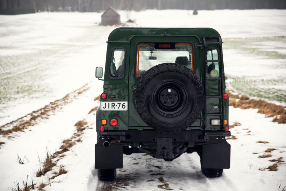 Green SUV on snowy trail near wooden barn