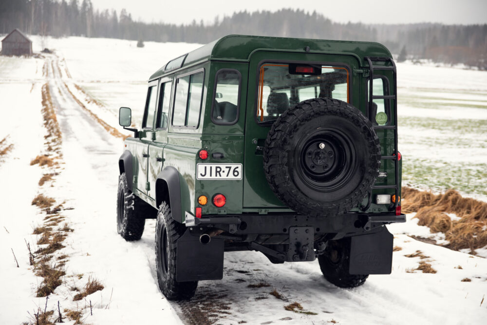 Green SUV on snowy rural road near wooden barn