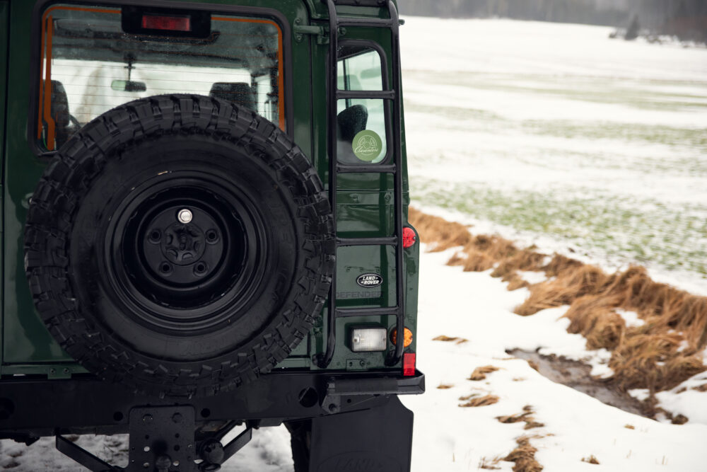 Green SUV with rear-mounted spare tire in snowy field