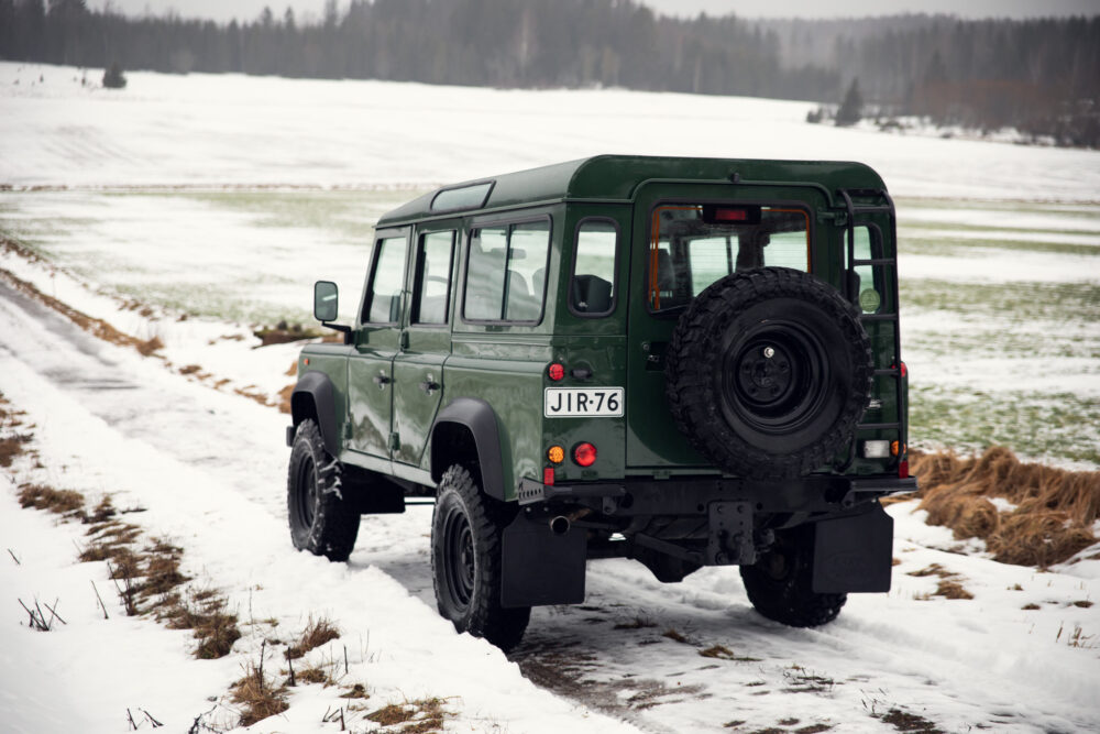 Green SUV on snowy field with sparse vegetation