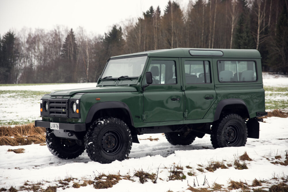 Green off-road SUV on snowy field near forest