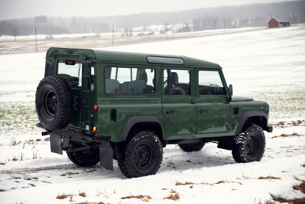 Green SUV in snowy field near red barn