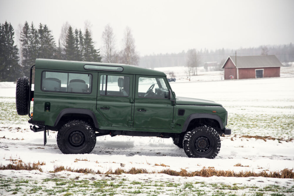 Green SUV in snowy field near barn