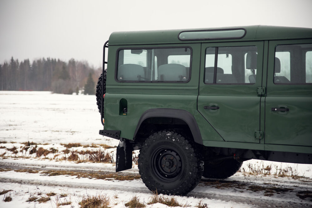 Green SUV parked on snowy field near forest